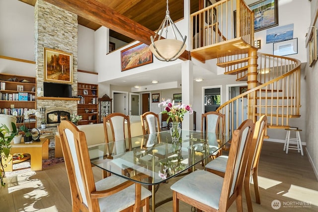 dining area with beam ceiling, a fireplace, a towering ceiling, wood finished floors, and stairs