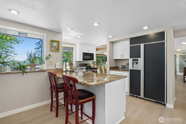 kitchen featuring black microwave, paneled built in refrigerator, a peninsula, white cabinets, and stainless steel electric range