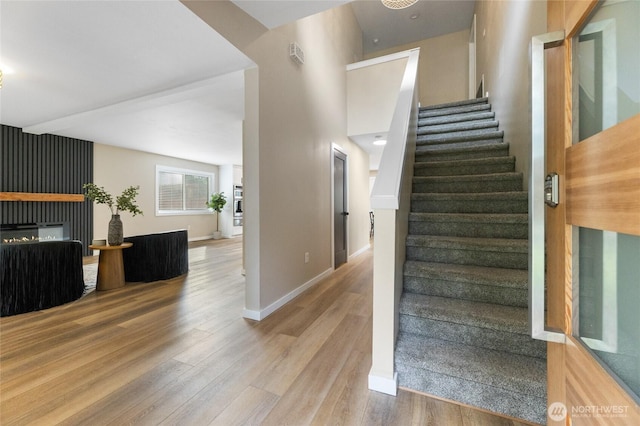 stairway with baseboards, wood finished floors, and a glass covered fireplace