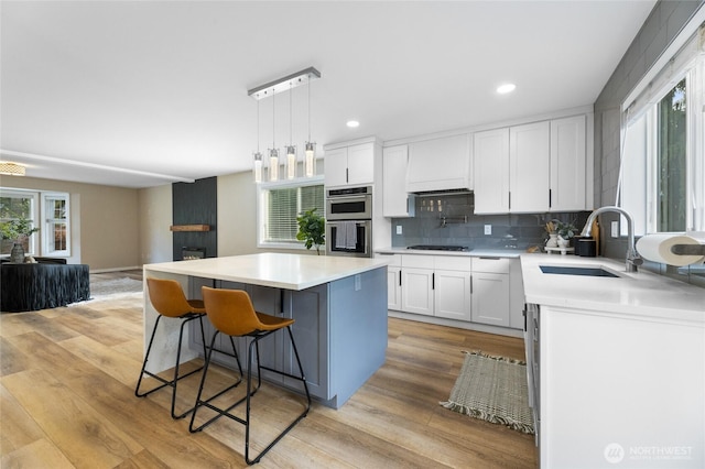 kitchen with a sink, white cabinetry, light countertops, hanging light fixtures, and a center island