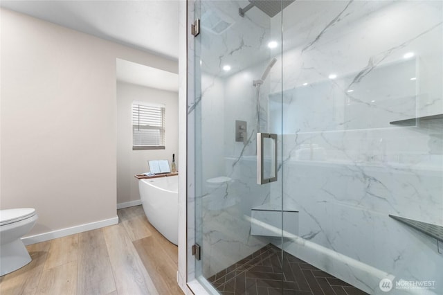 bathroom featuring a marble finish shower, toilet, wood finished floors, a freestanding tub, and baseboards