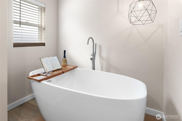 bathroom with a soaking tub, baseboards, and wood finished floors