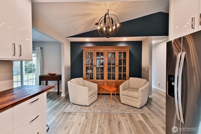 sitting room with light wood-style floors, a notable chandelier, vaulted ceiling, and baseboards