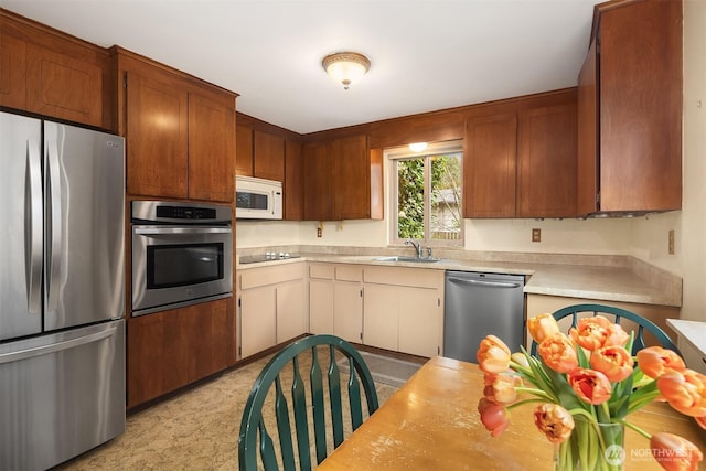 kitchen with appliances with stainless steel finishes, brown cabinetry, light countertops, and a sink