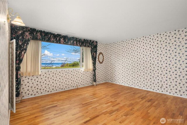 unfurnished room with baseboards, light wood-type flooring, and wallpapered walls