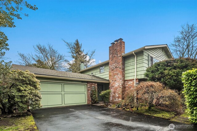 view of property exterior with a garage, driveway, brick siding, and a chimney