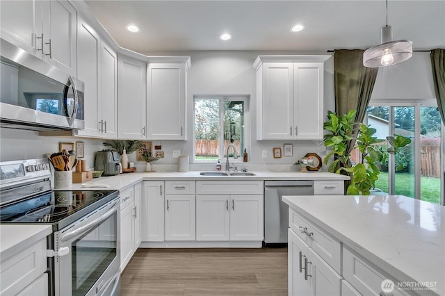 kitchen with white cabinets, light wood-style flooring, hanging light fixtures, stainless steel appliances, and a sink