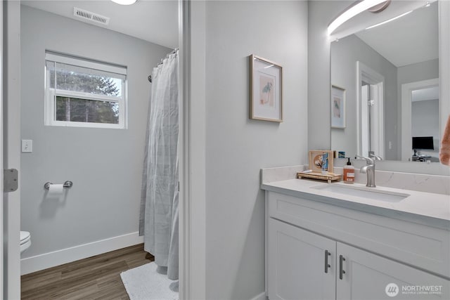 bathroom featuring toilet, wood finished floors, vanity, visible vents, and baseboards