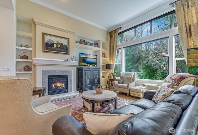 living room featuring built in features, wood finished floors, crown molding, and a glass covered fireplace