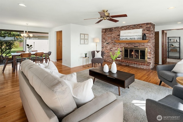 living room featuring recessed lighting, baseboards, wood finished floors, a fireplace, and ceiling fan with notable chandelier