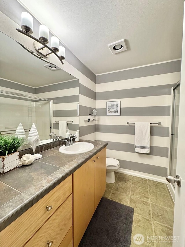 bathroom with a textured ceiling, toilet, vanity, and a shower with door