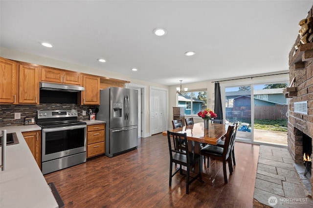 kitchen with a fireplace, dark hardwood / wood-style flooring, decorative light fixtures, backsplash, and appliances with stainless steel finishes