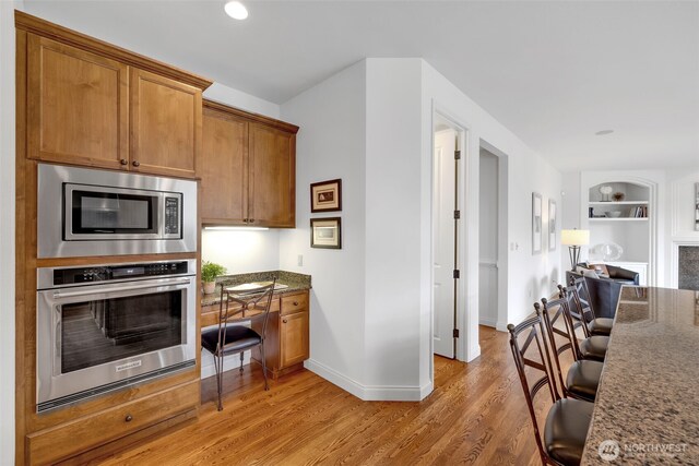 kitchen featuring built in shelves, stainless steel appliances, light wood-style floors, built in study area, and brown cabinets