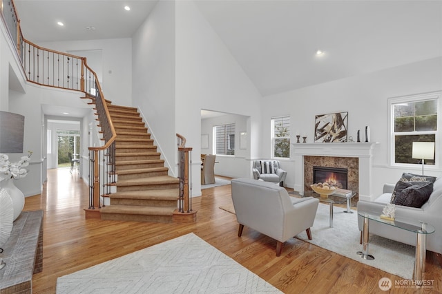 living room with high vaulted ceiling, stairway, light wood-type flooring, and a high end fireplace