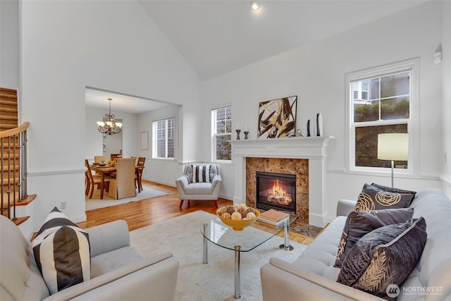 living area with stairway, high vaulted ceiling, light wood-style floors, a fireplace, and a chandelier