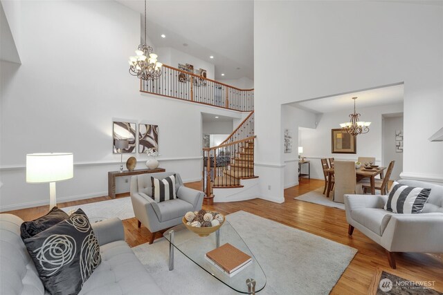 living room with a towering ceiling, light wood-style flooring, stairway, a chandelier, and recessed lighting