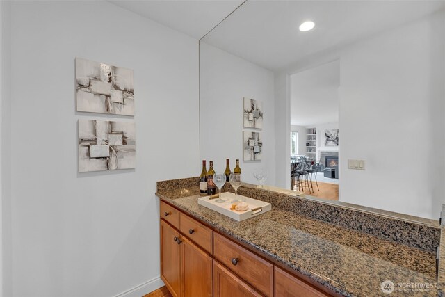 bathroom featuring a glass covered fireplace, vanity, baseboards, and recessed lighting