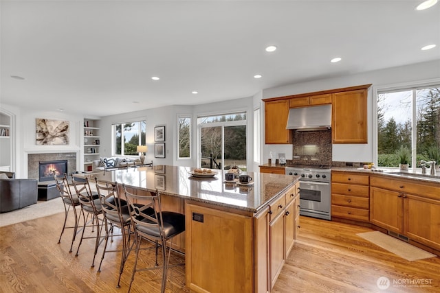 kitchen featuring stainless steel range, open floor plan, a kitchen island, light stone countertops, and under cabinet range hood