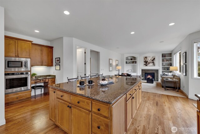 kitchen with light wood finished floors, open floor plan, dark stone countertops, a center island, and stainless steel appliances