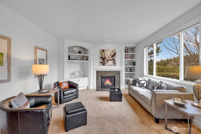 living area featuring built in shelves, light carpet, and a fireplace with flush hearth