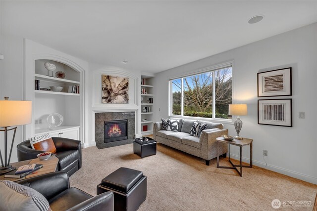 living area with light carpet, baseboards, built in features, and a glass covered fireplace