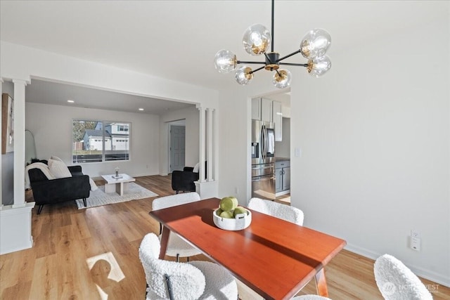 dining space with decorative columns, a chandelier, and light hardwood / wood-style flooring