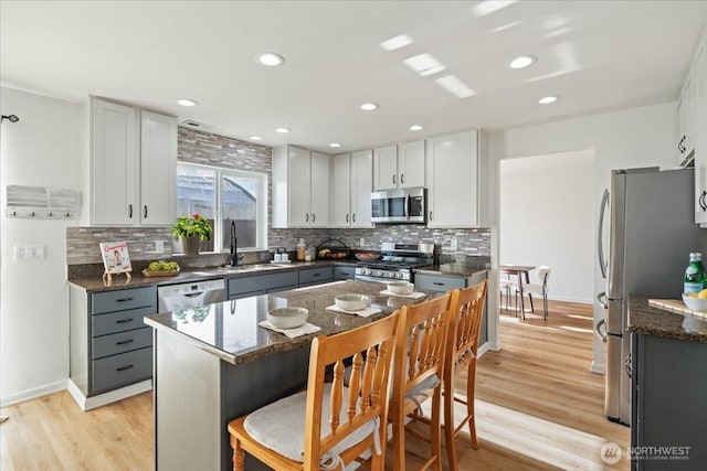 kitchen with gray cabinetry, stainless steel appliances, a kitchen island, sink, and dark stone countertops