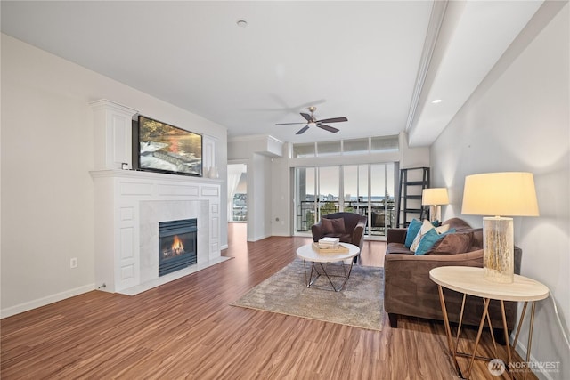 living area with a fireplace with flush hearth, ceiling fan, baseboards, and wood finished floors