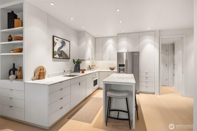 kitchen with a kitchen island, light stone counters, white oven, stainless steel refrigerator with ice dispenser, and a sink