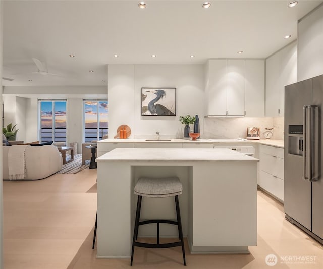 kitchen with high end fridge, light countertops, white cabinetry, a kitchen island, and a sink