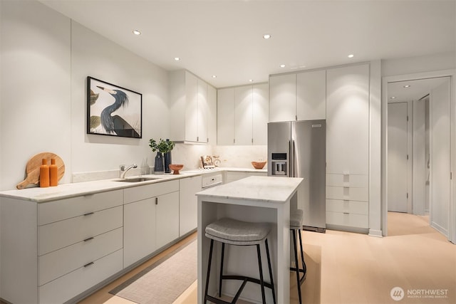 kitchen featuring stainless steel fridge with ice dispenser, a kitchen island, a sink, light wood-type flooring, and a kitchen breakfast bar