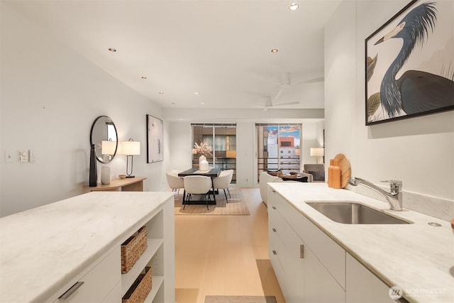 kitchen with a ceiling fan, light countertops, light wood-style floors, white cabinetry, and a sink