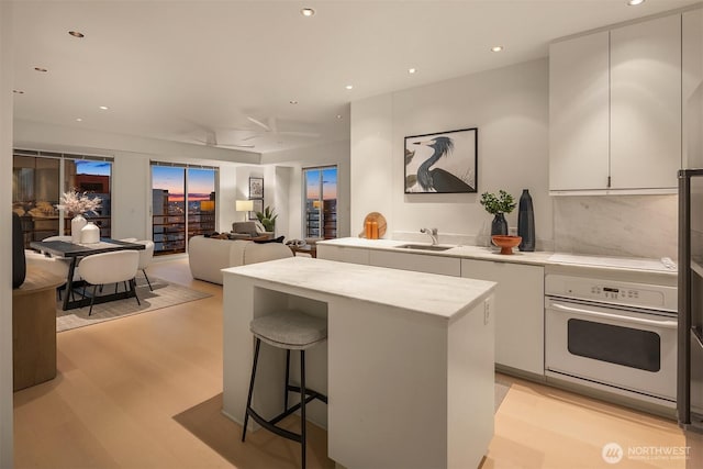 kitchen featuring a center island, white oven, cooktop, white cabinetry, and a sink