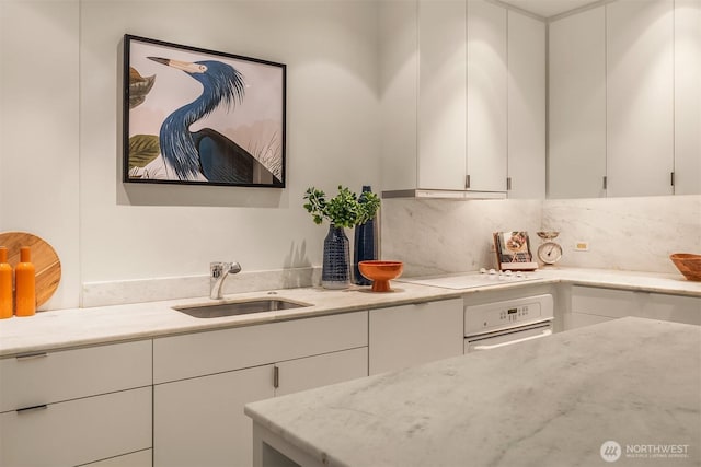 kitchen featuring white appliances, light stone counters, under cabinet range hood, white cabinetry, and a sink