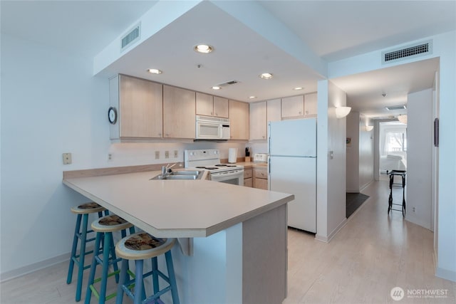 kitchen featuring sink, kitchen peninsula, white appliances, and a kitchen bar