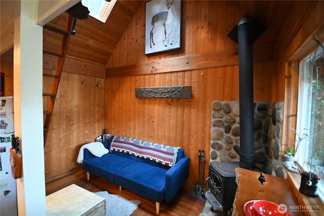 sitting room with vaulted ceiling with skylight, a wood stove, wood walls, and wood finished floors