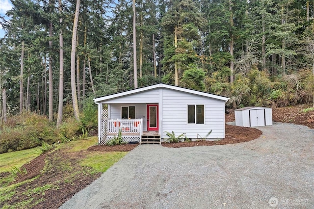 view of front facade featuring an outbuilding, covered porch, a view of trees, a shed, and driveway