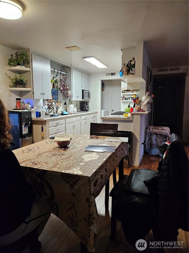 kitchen with light wood-type flooring, white cabinetry, and stainless steel microwave