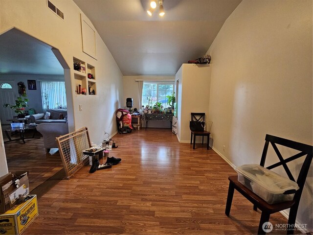hallway featuring vaulted ceiling, baseboards, arched walkways, visible vents, and wood finished floors
