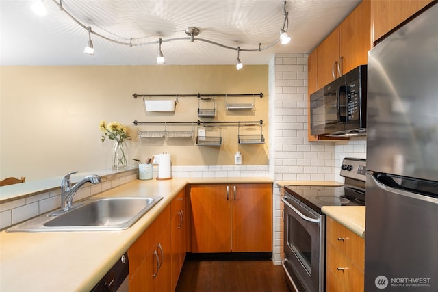 kitchen with brown cabinetry, decorative backsplash, appliances with stainless steel finishes, light countertops, and a sink