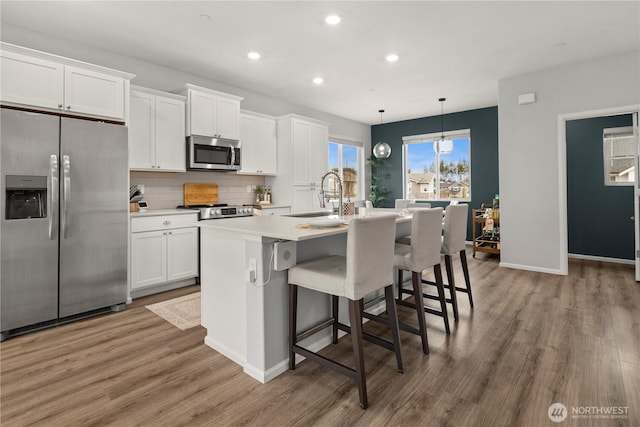 kitchen with a sink, white cabinets, light countertops, appliances with stainless steel finishes, and an island with sink