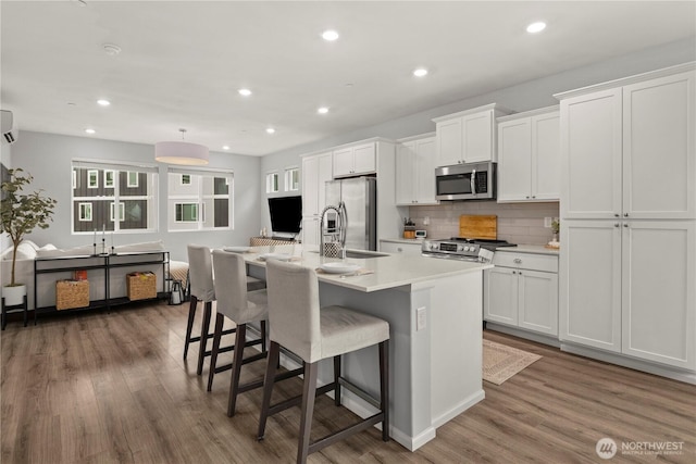 kitchen with stainless steel appliances, a sink, white cabinets, light countertops, and an island with sink