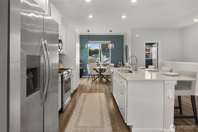 kitchen featuring stainless steel appliances, a sink, a kitchen island with sink, and white cabinets