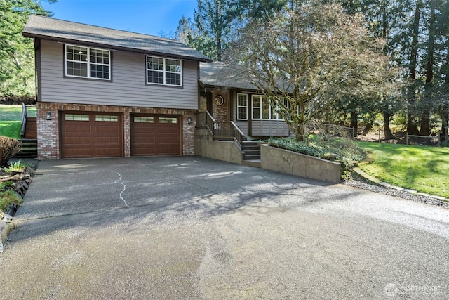 split level home featuring a garage, brick siding, and aphalt driveway