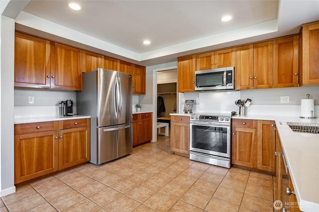 kitchen with sink, stainless steel appliances, a tray ceiling, and light tile patterned floors