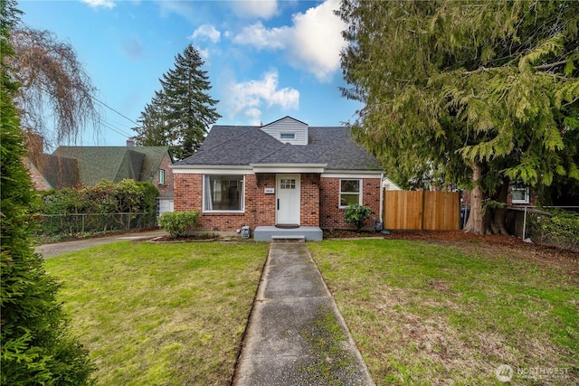 view of front of home featuring roof with shingles, brick siding, a front lawn, and fence private yard