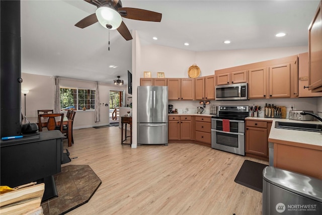 kitchen with light wood-type flooring, a wood stove, stainless steel appliances, sink, and ceiling fan