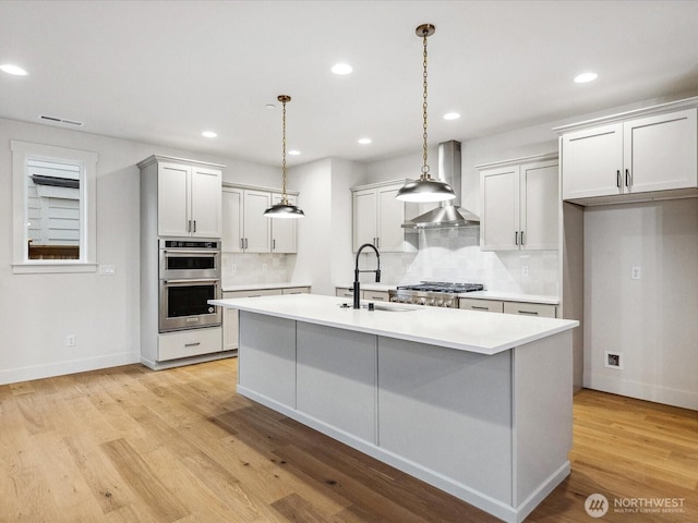 kitchen with stainless steel double oven, a sink, light countertops, a center island with sink, and pendant lighting