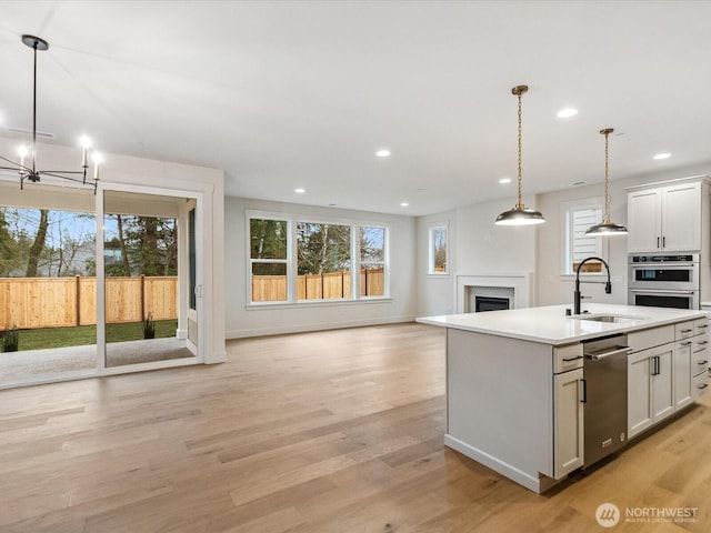 kitchen featuring light countertops, hanging light fixtures, open floor plan, a sink, and an island with sink