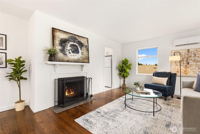 living area featuring a brick fireplace, an AC wall unit, dark wood finished floors, and baseboards